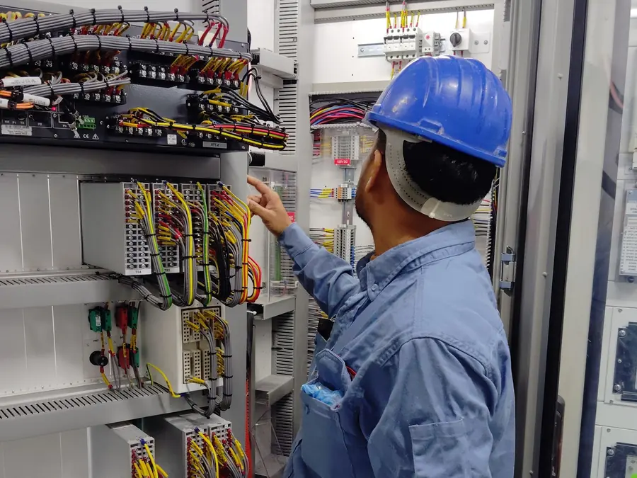 Eletricista de uniforme azul testando um quadro de energia com medidor