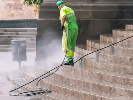 Profissional de uniforme verde lavando uma escada de pedra com jato de água