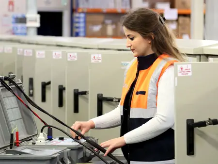 Eletricista de colete laranja operando um painel de energia