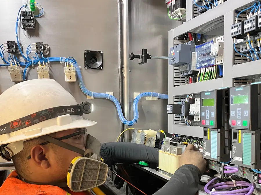 Eletricista de capacete e máscara trabalhando em um quadro de disjuntores